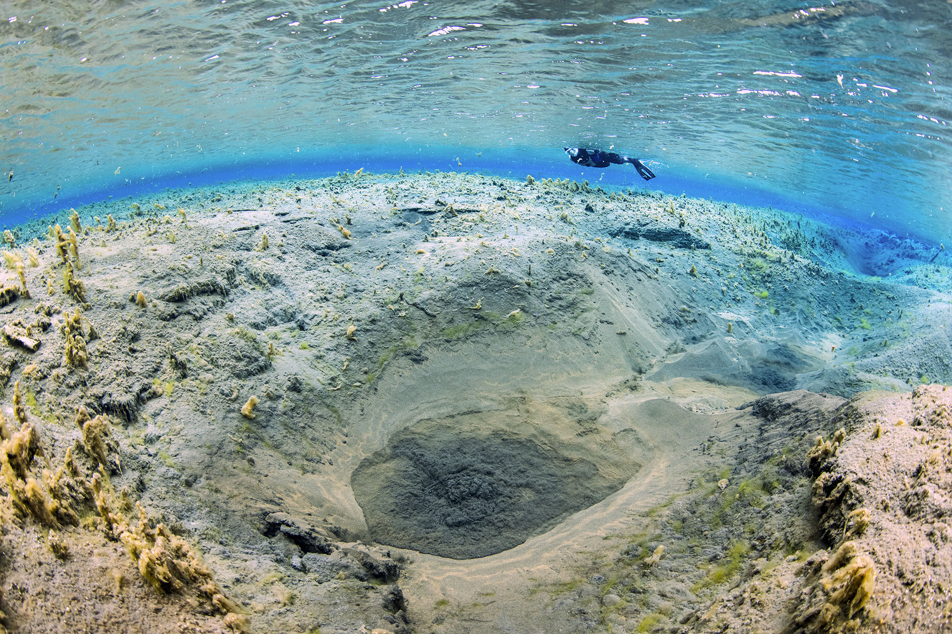 Diver exploring underwater blue hole and landscape, surrounded by clear water and marine life.