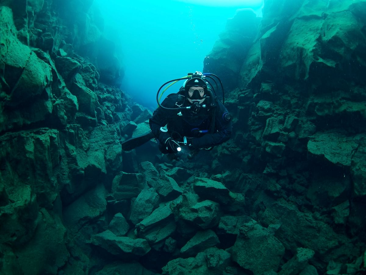 Scuba diver exploring underwater rock formations in clear, blue water.