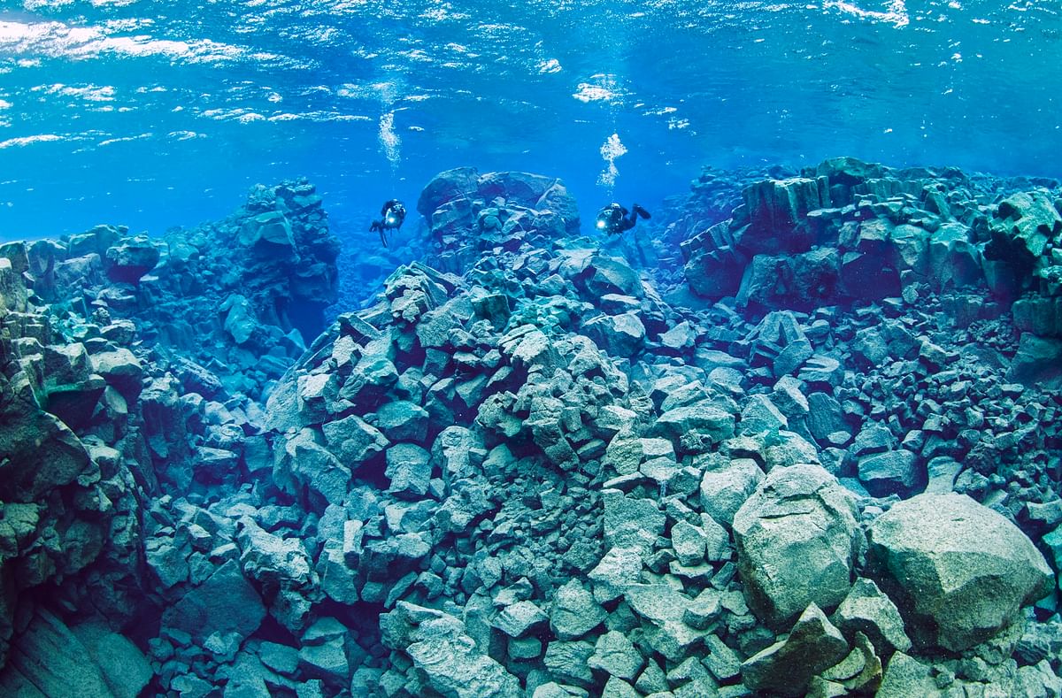 Divers exploring underwater rocky terrain in clear blue water.