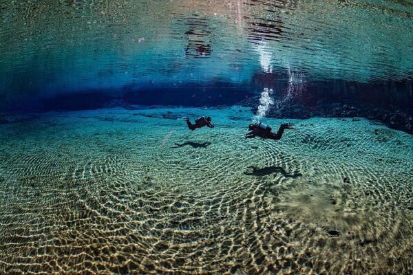 Divers exploring a clear underwater world, surrounded by rippling sand and vibrant blue tones, capturing adventure.