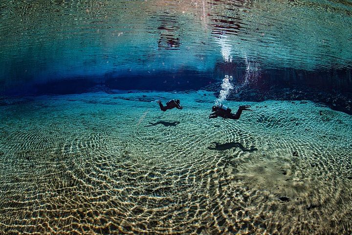 Divers exploring a clear underwater world, surrounded by rippling sand and vibrant blue tones, capturing adventure.