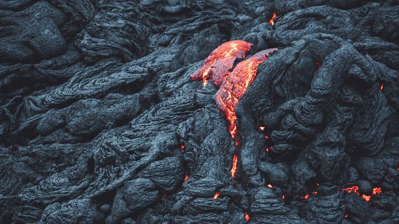 Molten lava flowing over black volcanic rock, showcasing bright red and orange hues against a dark textured surface.