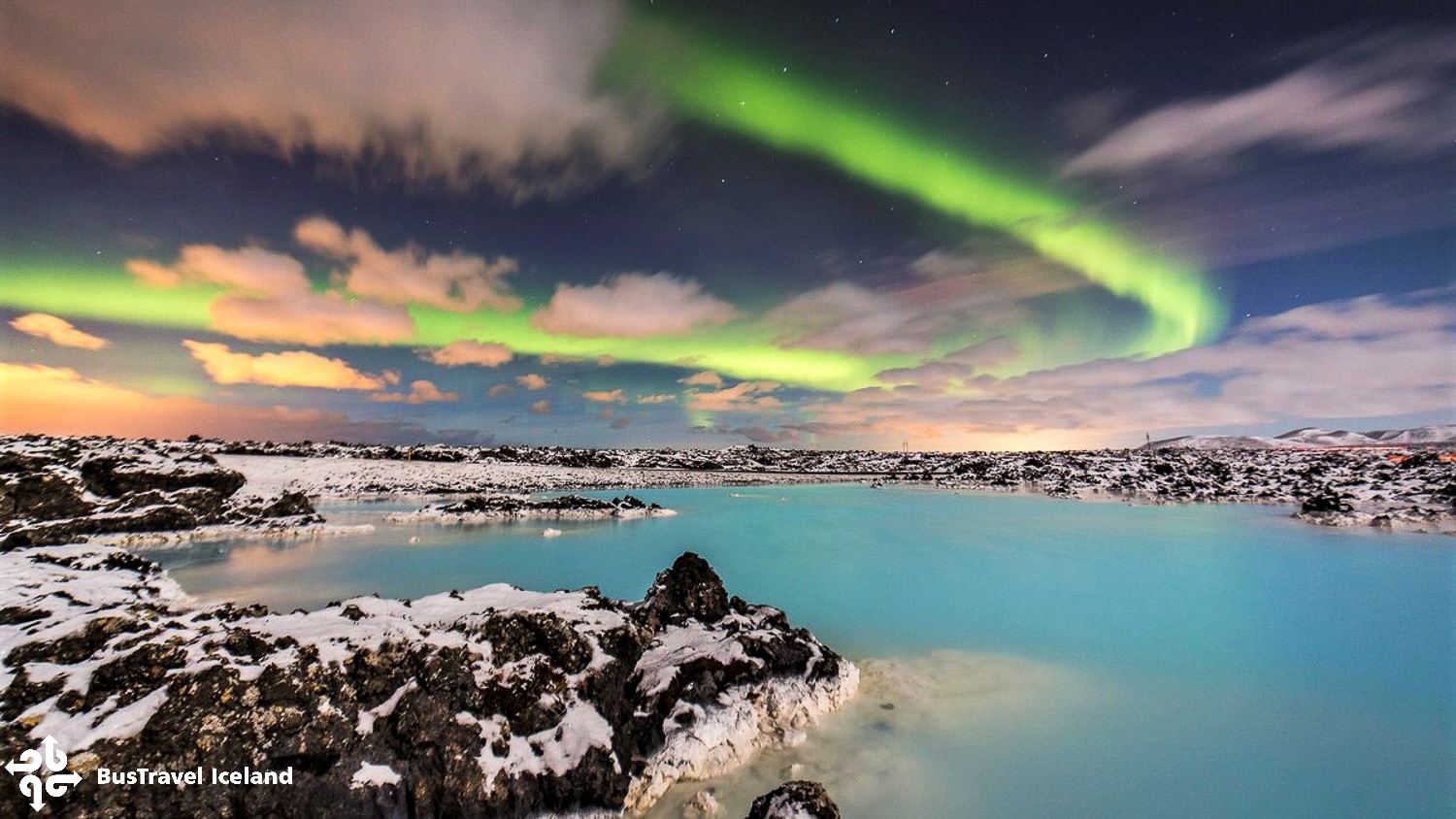 Northern Lights over snowy Icelandic landscape and blue lagoon at night.