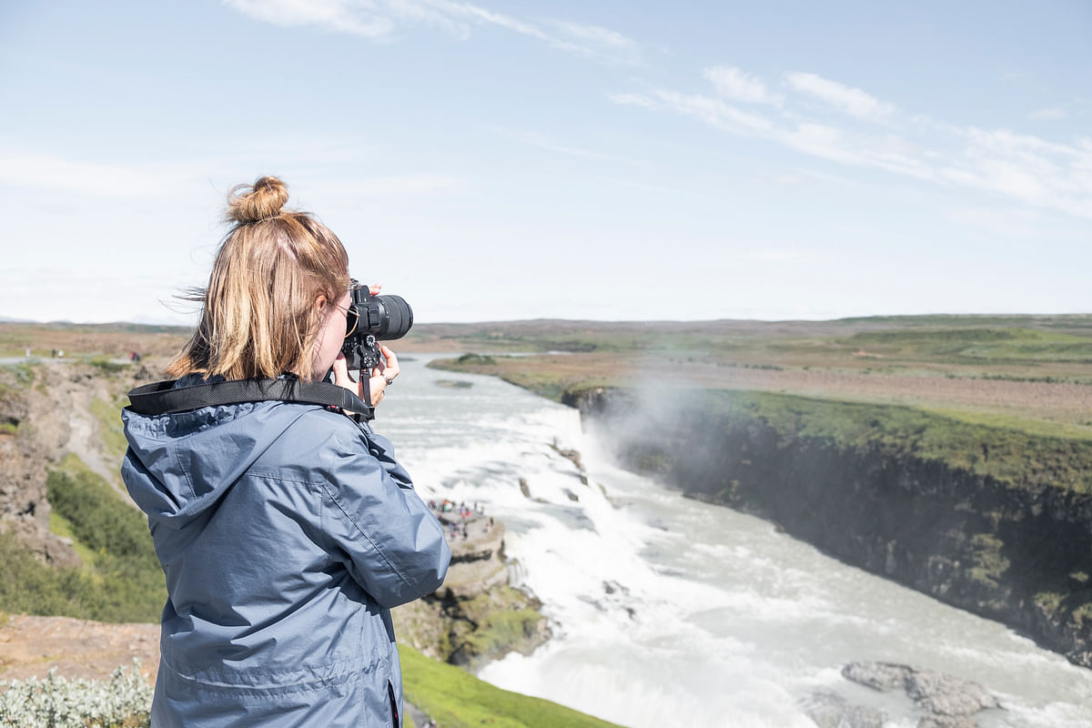 Photographer capturing stunning waterfall landscape in Iceland on a clear day.