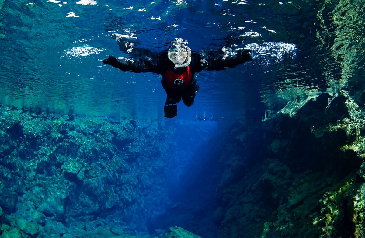 Snorkeler explores underwater landscape with clear blue water and rocky terrain.