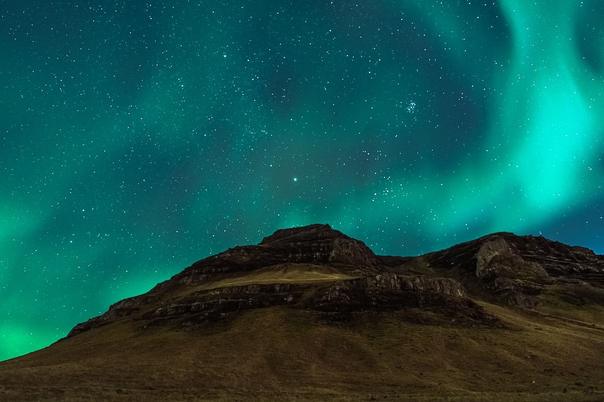 Northern lights over dark rocky hill, starry sky illuminating landscape with emerald aurora borealis display.