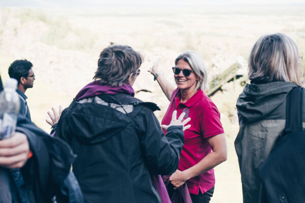 Group of people socializing outdoors, woman in pink shirt smiling, enjoying nature background.