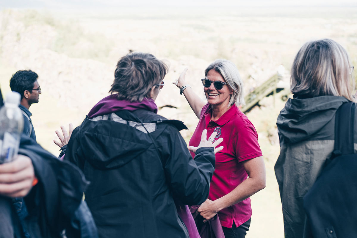 Group of people socializing outdoors, woman in pink shirt smiling, enjoying nature background.