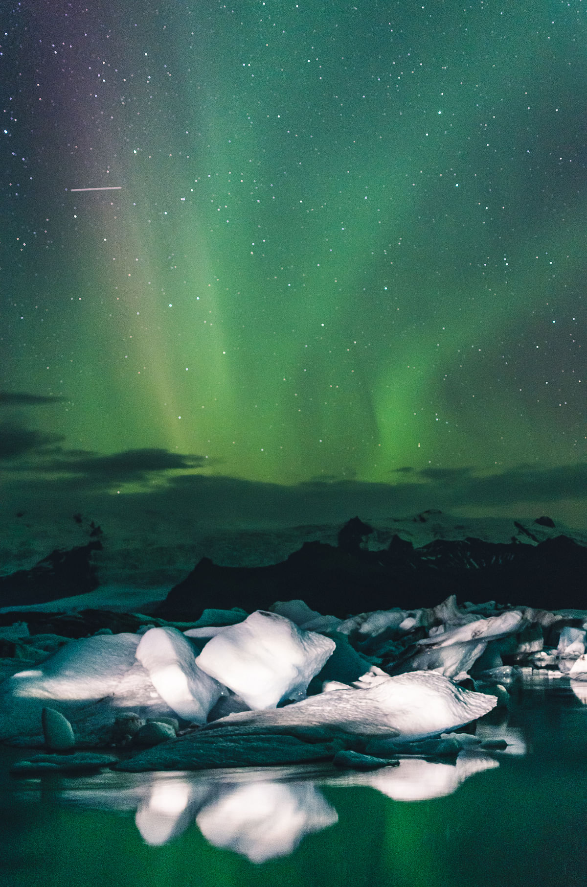 Northern Lights over icy landscape with stars, reflecting on water at night.