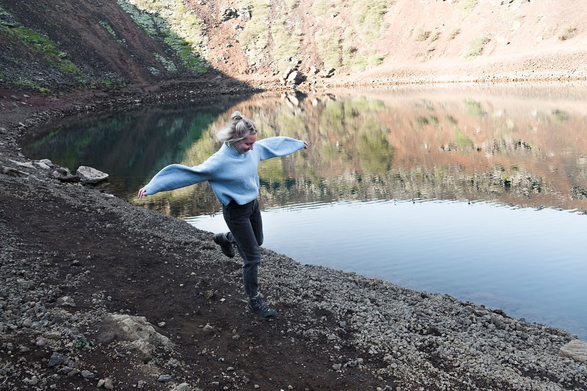 Person joyfully running beside a reflective lake in a scenic rocky landscape.