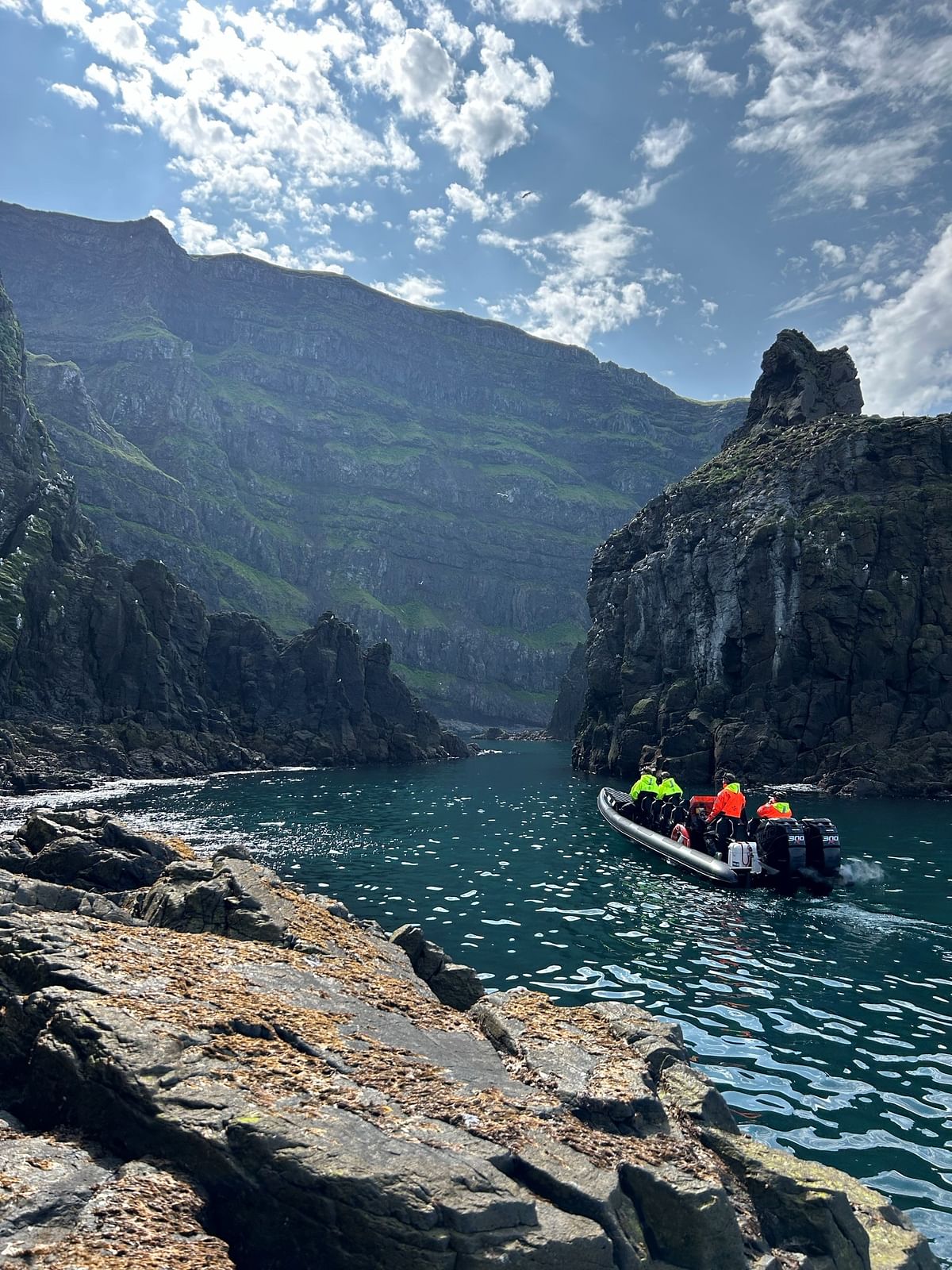 Boat navigating through rocky coastal cliffs under a partly cloudy sky.