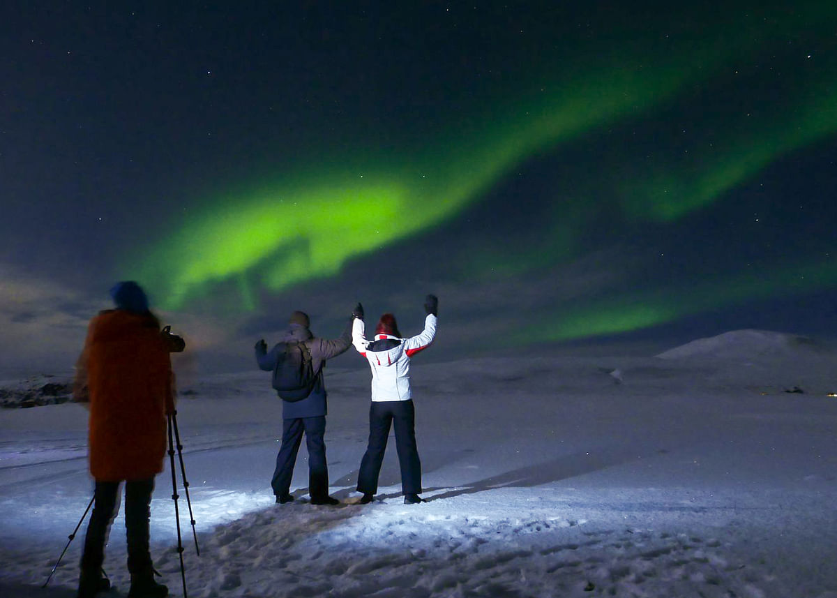 People observing the Northern Lights in snowy landscape, with a photographer capturing the aurora borealis.