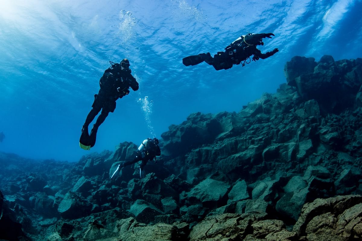 Scuba divers exploring underwater rocks in clear blue ocean depths.