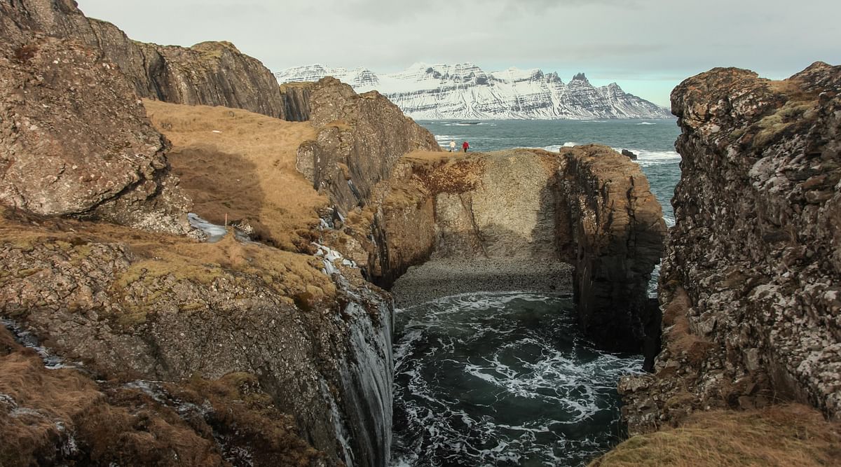 Majestic coastal cliffs with rugged rocks and snowy mountains in the background, Icelandic landscape scenery.