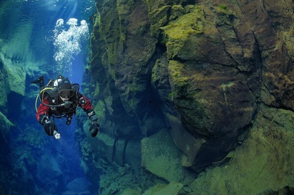Scuba diver exploring underwater canyon with rocky walls and clear water.