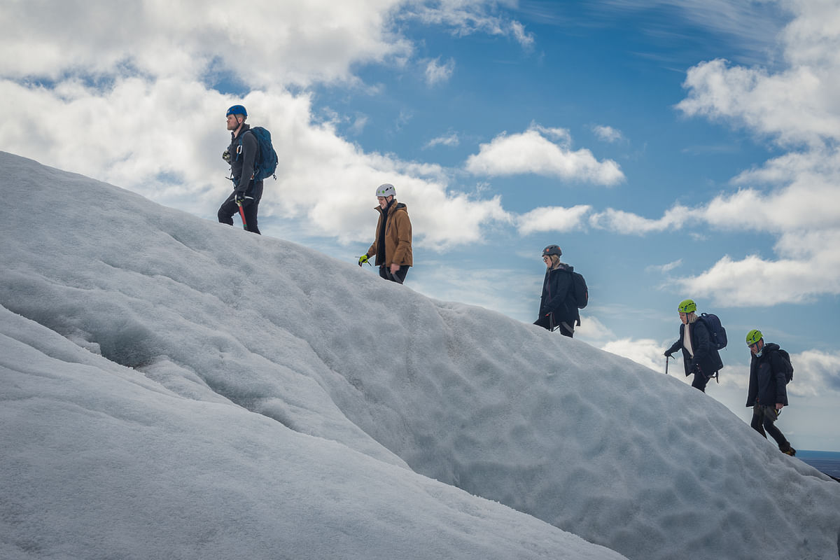 Group of climbers hiking up a snowy slope under a clear sky, wearing helmets and backpacks.