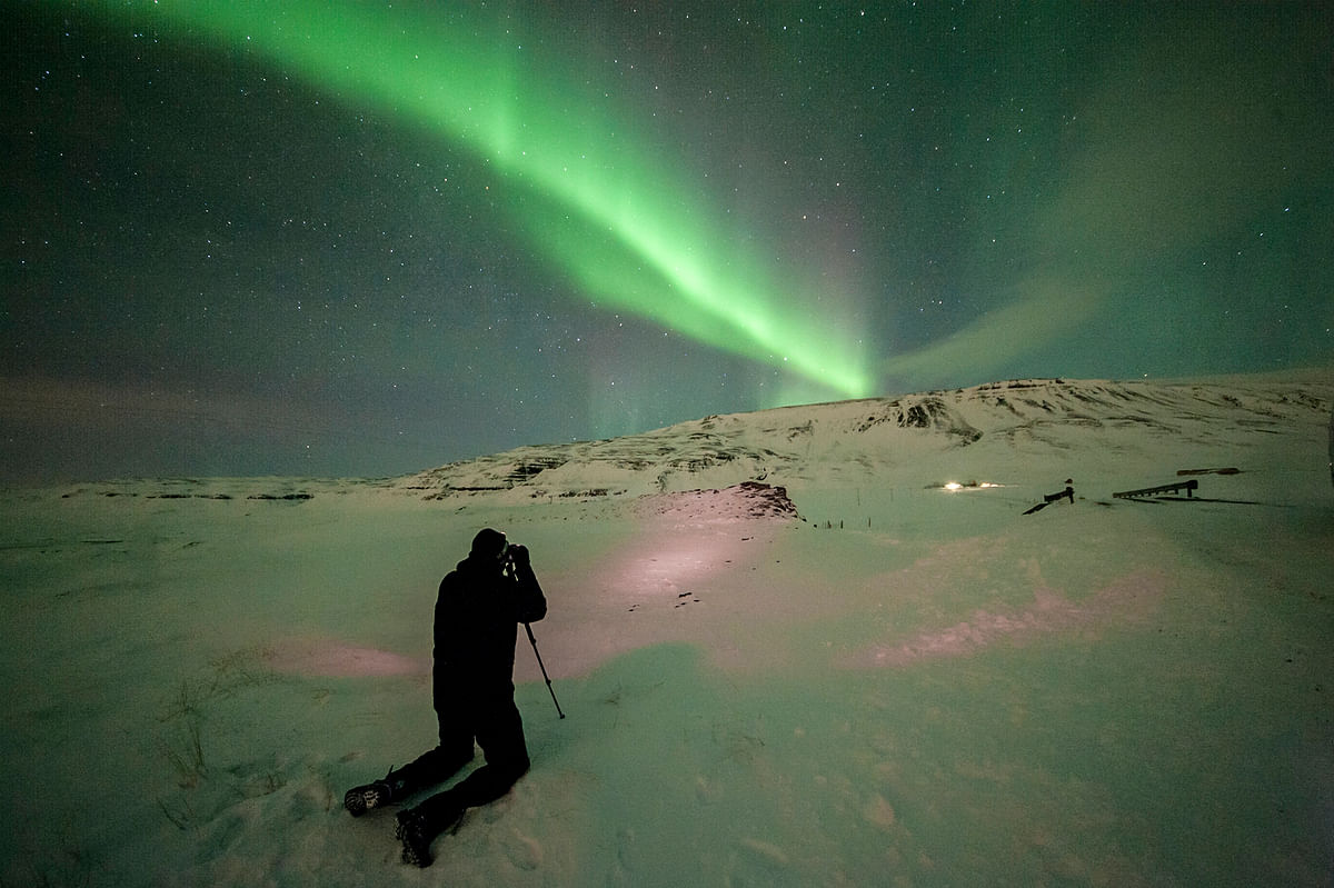 Photographer captures stunning Northern Lights over snowy landscape at night.