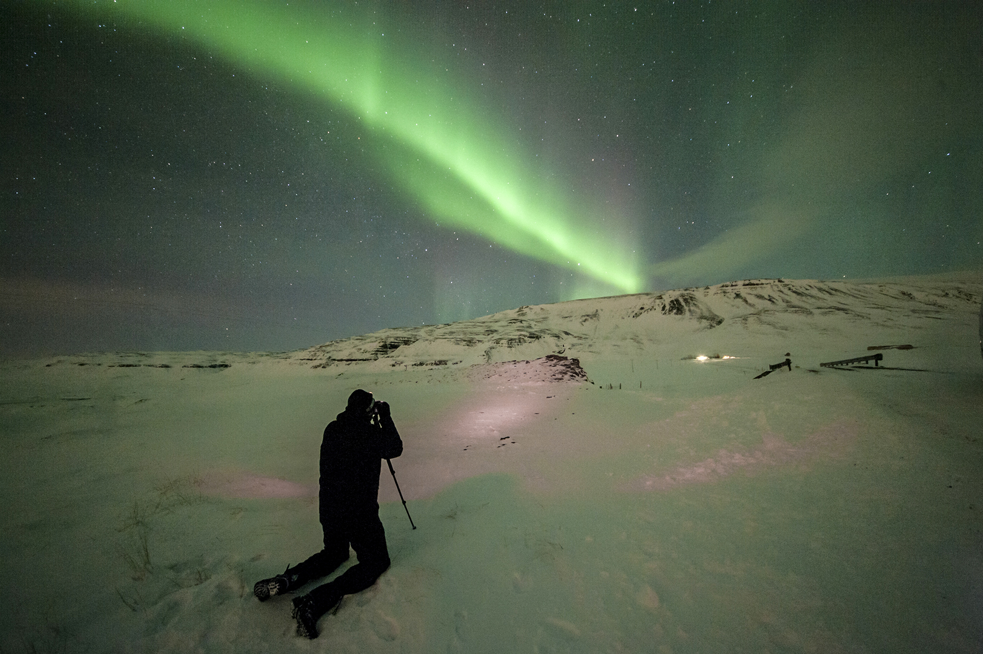 Photographer capturing Northern Lights over snowy landscape at night, with vivid green aurora illuminating the sky.