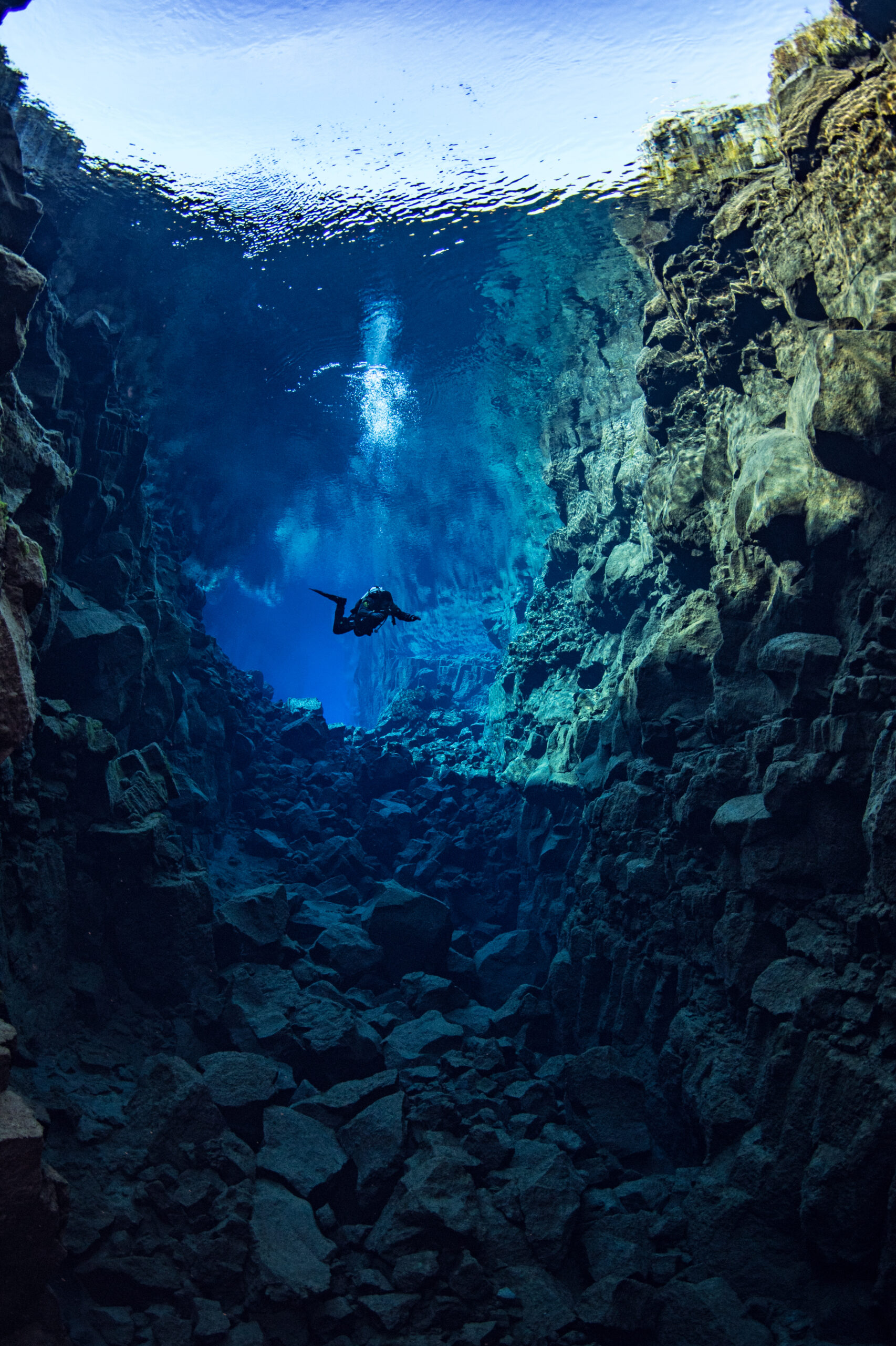 Scuba diver explores a deep underwater canyon with rocky walls and clear blue water.