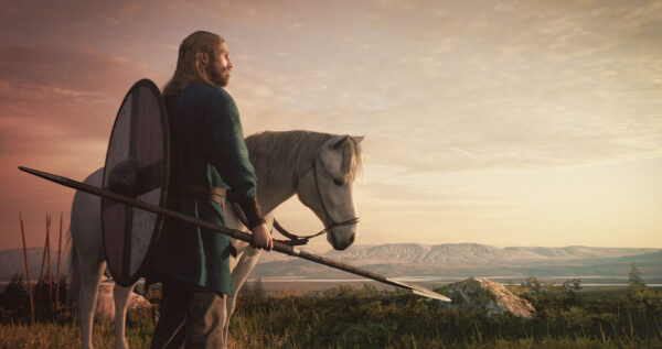 Medieval warrior with spear and shield standing beside a white horse in a scenic landscape during sunset.
