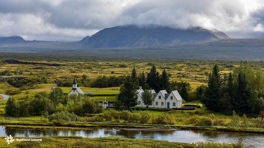 Scenic view of Icelandic countryside with historic church and houses surrounded by greenery and mountains in the background.