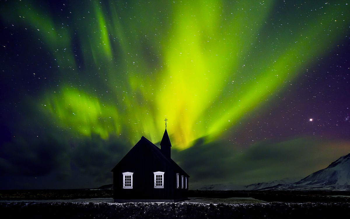 Northern lights illuminate a church silhouette against a starry night sky.