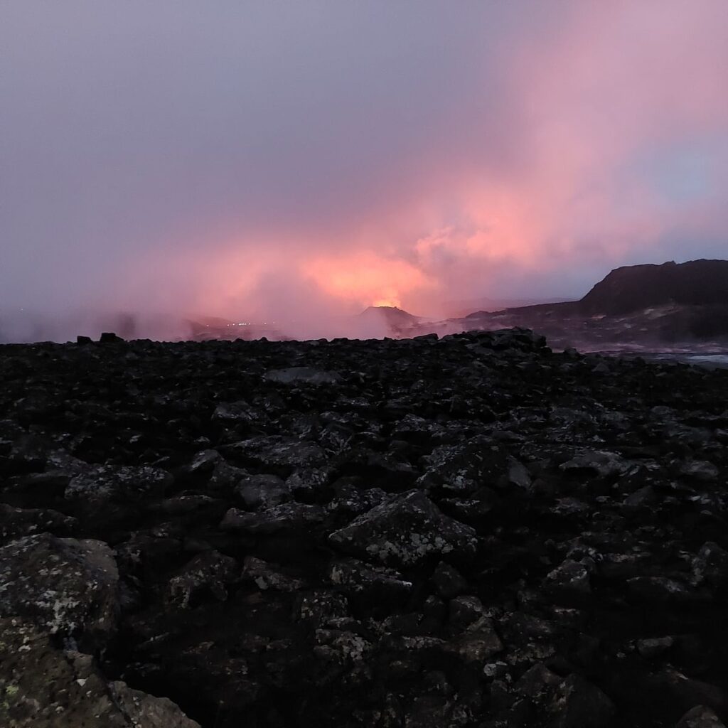 Volcanic landscape at dusk with a fiery sky and rocky terrain, creating a dramatic and serene atmosphere.
