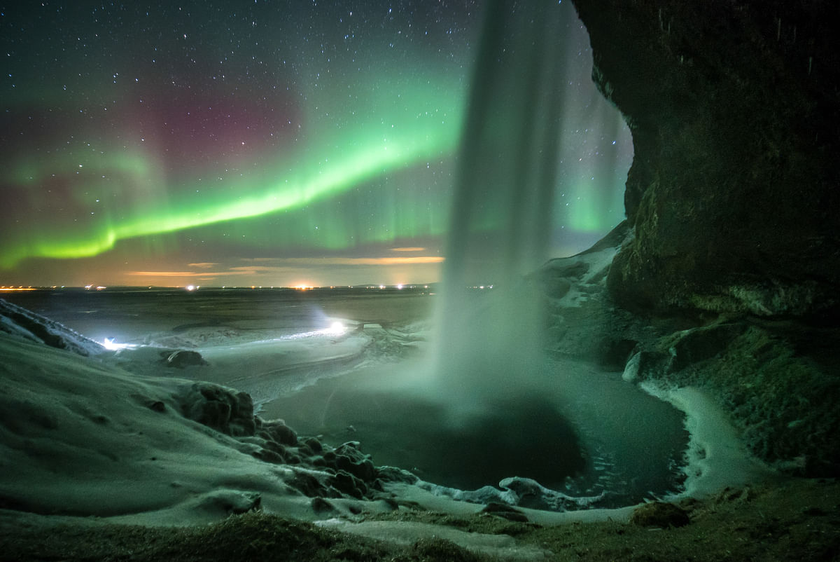 Northern lights above a waterfall, illuminating the icy landscape at night in a stunning natural display.