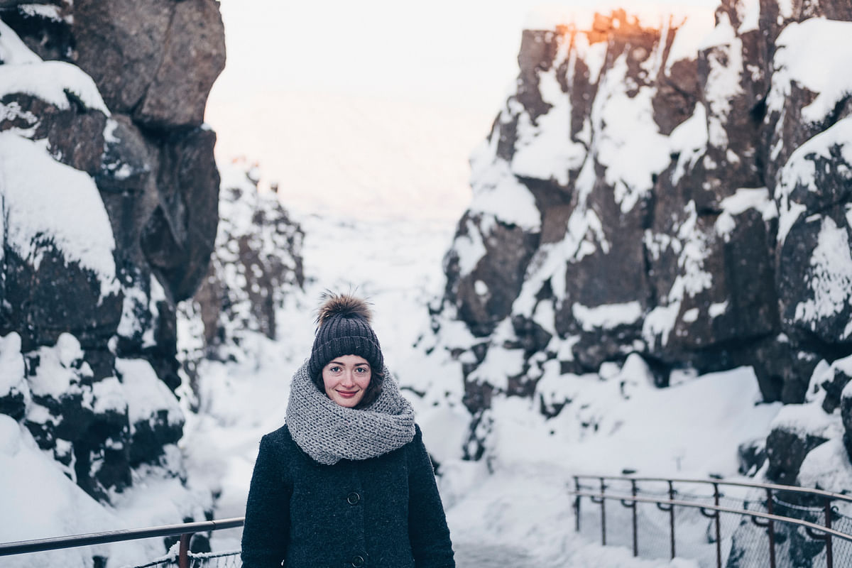 Person bundled up in winter attire stands in a snowy canyon landscape under a clear sky.