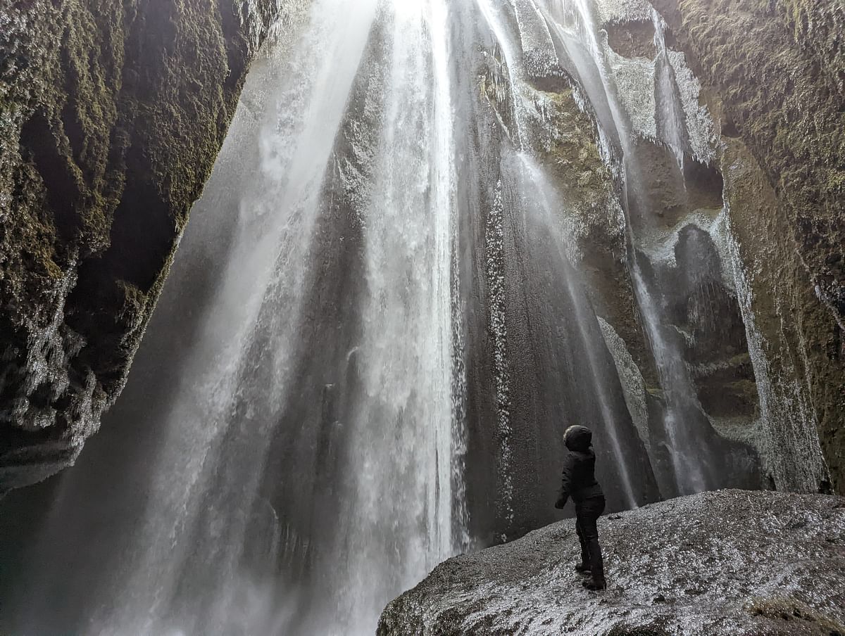 Person admiring a large waterfall cascading down mossy rocks, capturing nature's grandeur and power.