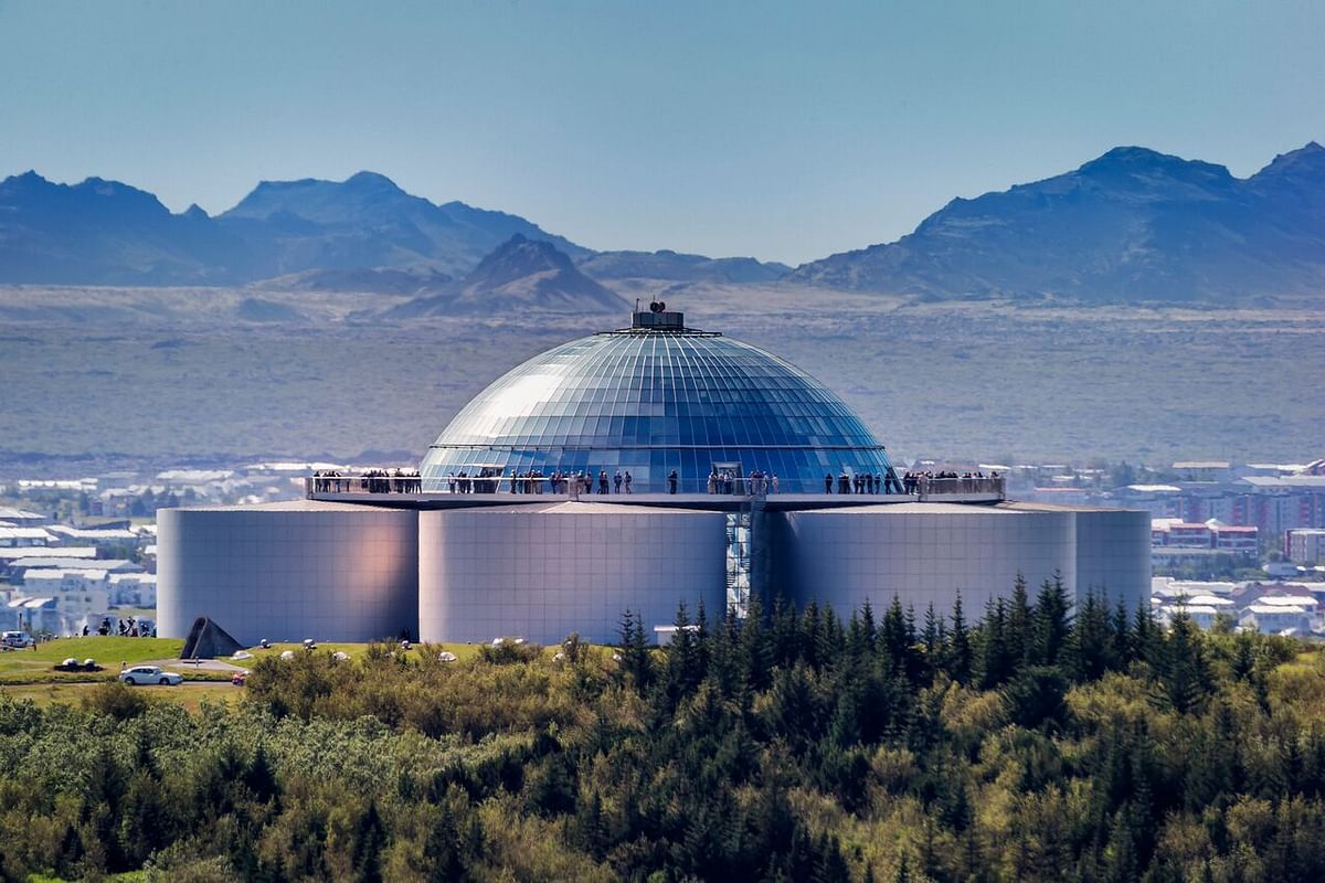 Futuristic glass-domed building in Reykjavik, Iceland, against a backdrop of mountains and urban landscape.