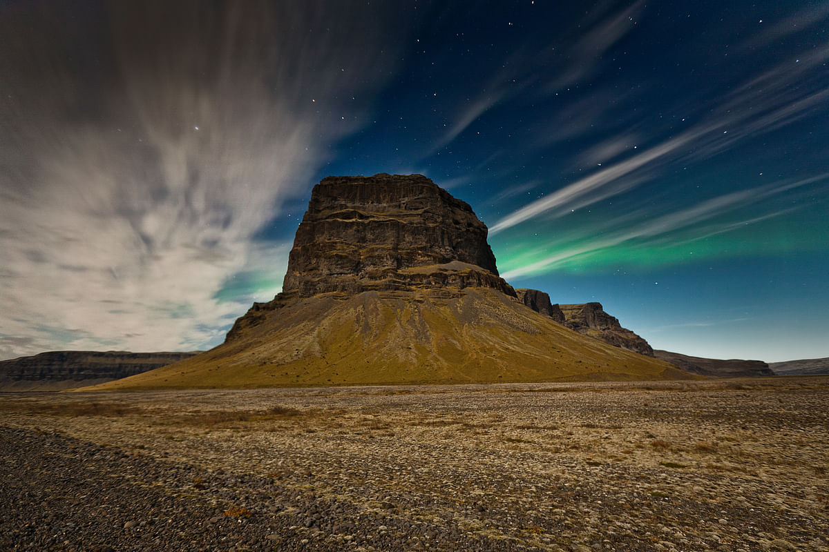 Majestic hill under a starry night sky with aurora borealis, offering a stunning landscape view.