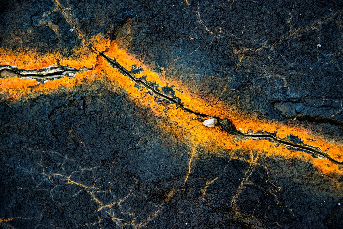 Cracked dark rock with bright orange mineral vein, resembling abstract art, showcasing nature's geological formations.