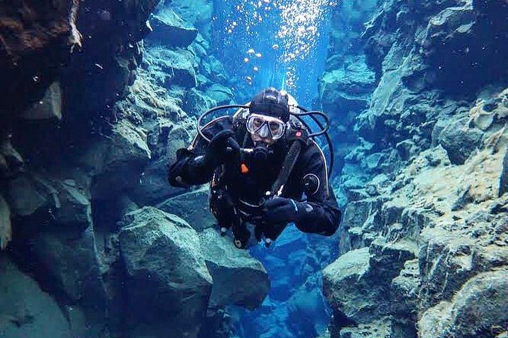 Scuba diver exploring underwater canyon with clear blue water and rocky walls, creating a stunning aquatic landscape.