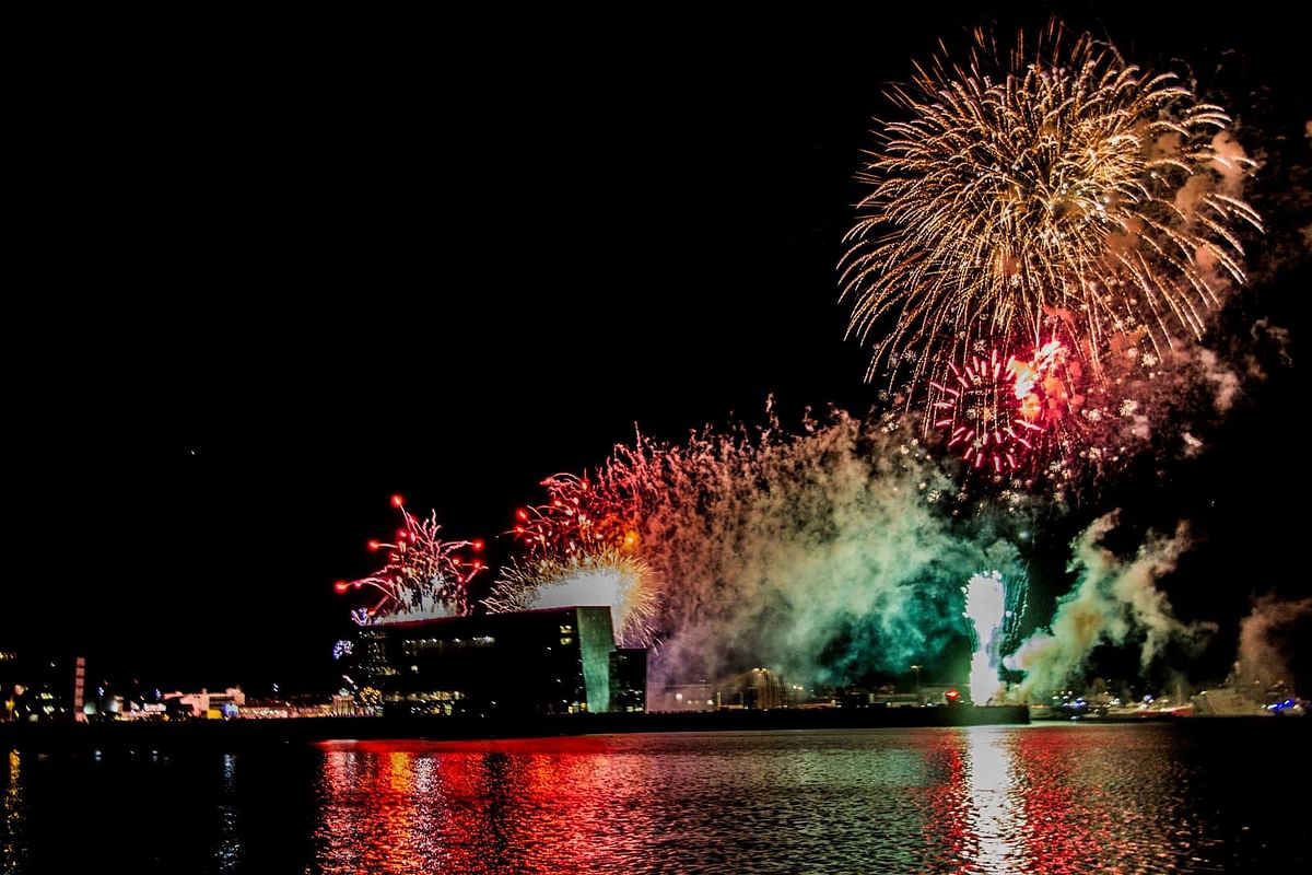 Vibrant fireworks light up the night sky over a waterfront cityscape, reflecting beautifully on the water.