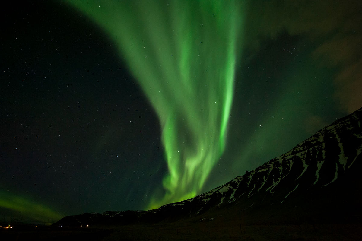 Vibrant green northern lights dance over a starry mountain landscape at night.