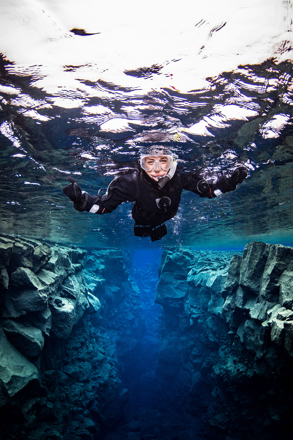Diver snorkeling in clear blue water between underwater rock formations.