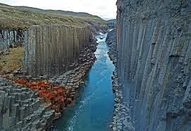 River flowing between dramatic basalt columns in Iceland, showcasing unique geological formations and vibrant waters.