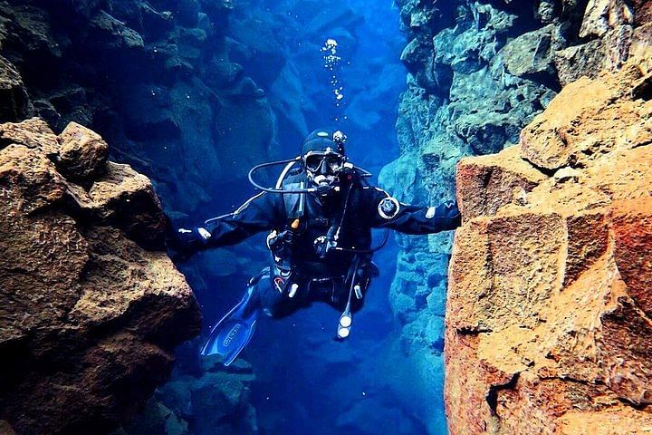 Scuba diver swims through underwater rock formation in clear blue waters.