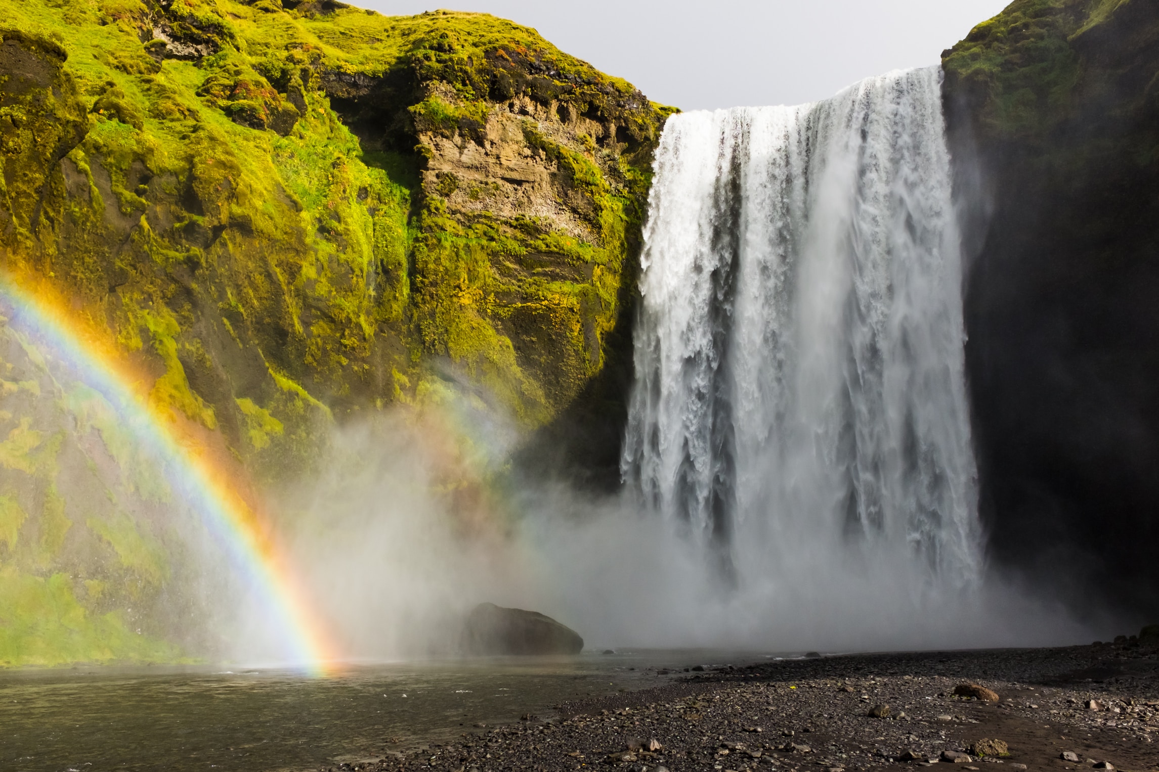 Waterfall cascading over mossy cliffs with a vibrant rainbow in the mist below.