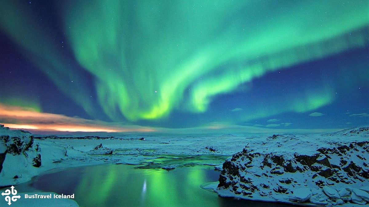 Spectacular Northern Lights over snowy Icelandic landscape and reflecting water.