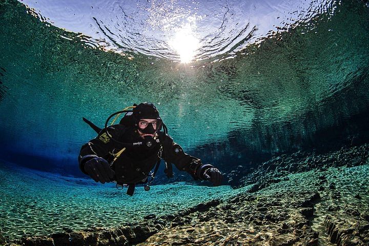 Scuba diver exploring crystal-clear underwater landscape with sunlight above, rocks and aquatic scenery.