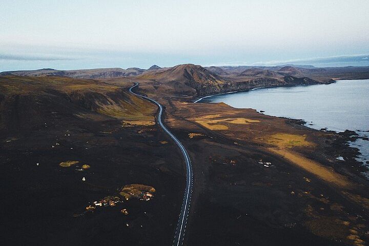 Aerial view of a scenic coastal road with mountains and ocean in Iceland, capturing the rugged natural beauty of the landscape.