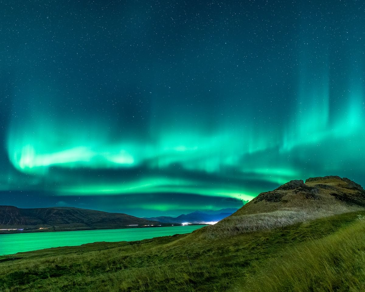 Aurora borealis over grassy landscape under starry sky, illuminating the night with vibrant green hues.