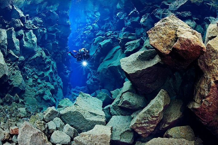 Scuba diver exploring underwater rock formations in clear blue water, capturing the beauty of underwater adventure.