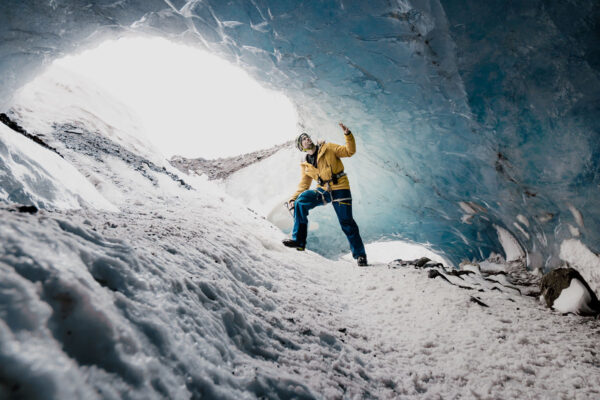 Person exploring icy cave interior, surrounded by blue ice walls and snow. Adventure and travel in winter landscape.
