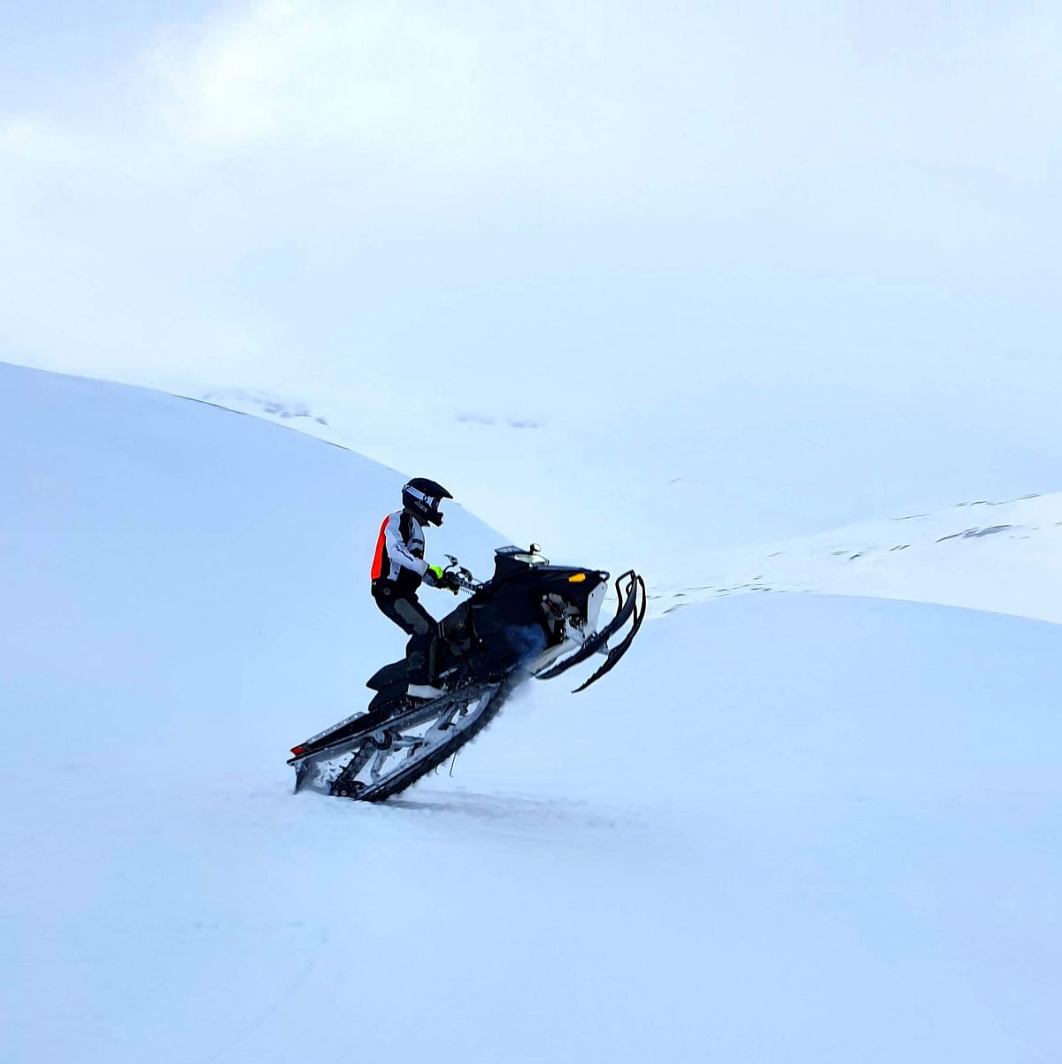 Snowmobiler ascending a snowy hill in winter gear, showcasing extreme sports adventure in a pristine snowy landscape.