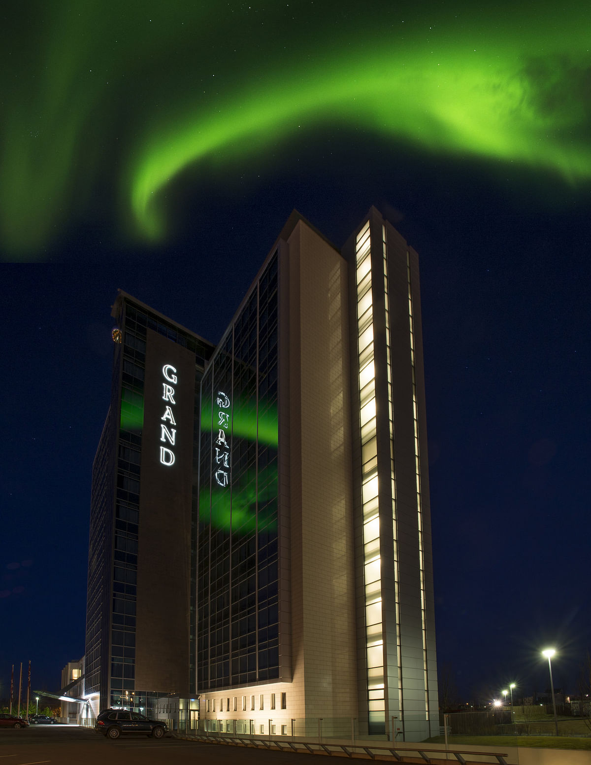 Tall hotel under vibrant northern lights in the night sky.