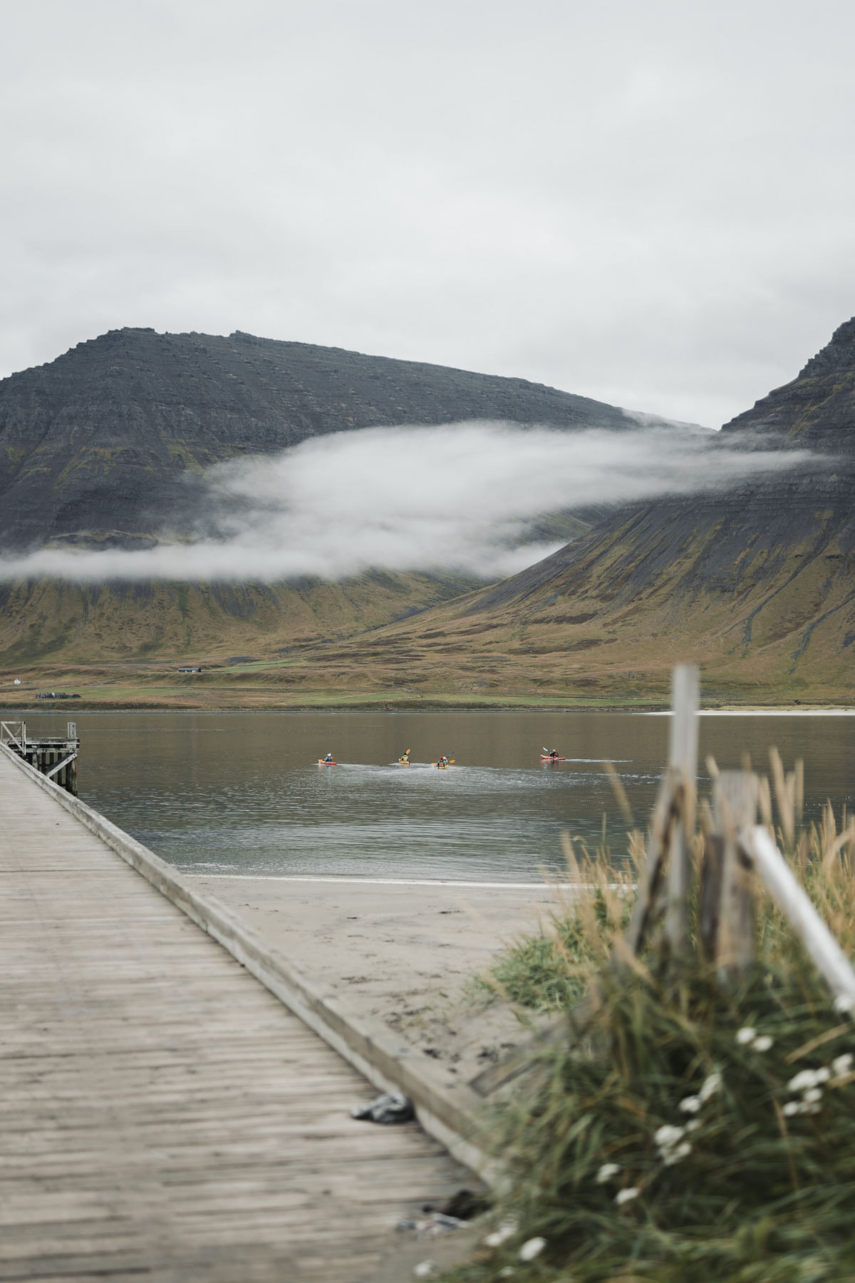 Kayakers on a serene lake with foggy mountains and a wooden dock in the foreground.