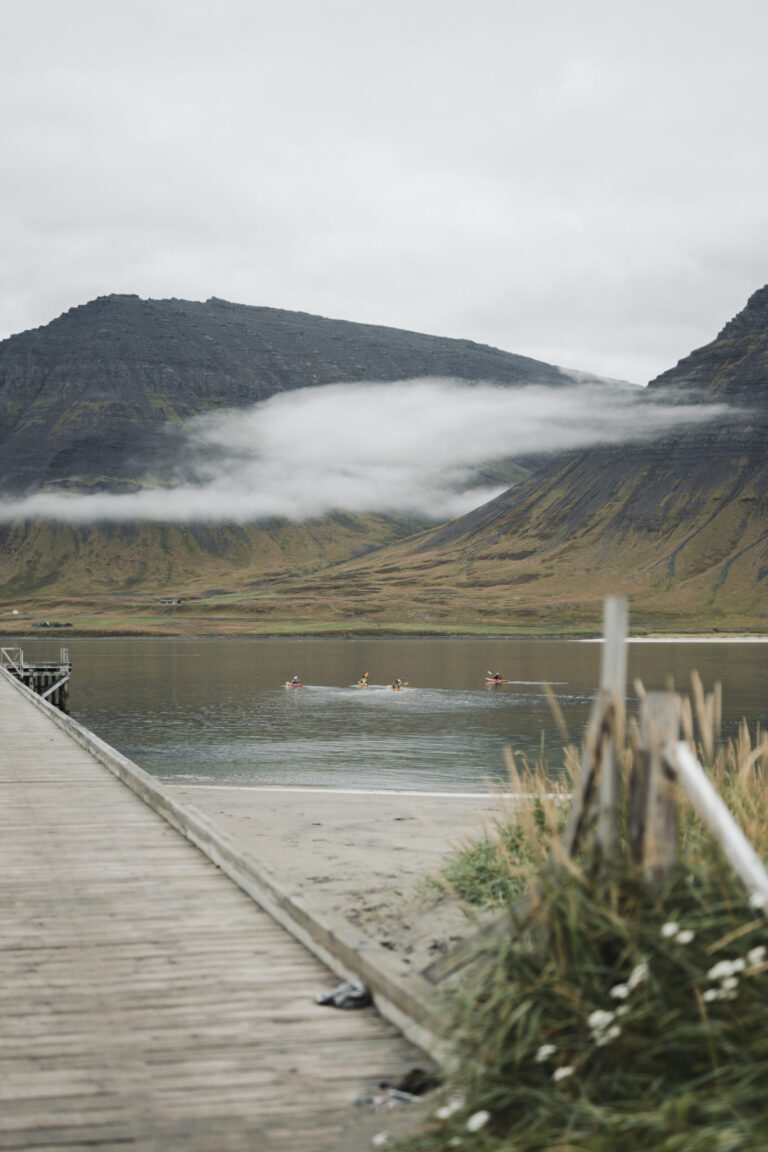 Kayakers paddling on a serene lake surrounded by misty mountains and a wooden dock.
